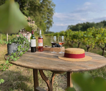 Table en bois décorée et disposée dans les vignes pour une dégustation champêtre avec des bouteilles de vin rouge et rosé du château
