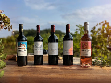 Photographie d'une table sur laquelle sont disposées des bouteilles de vin des Vignobles Bougès avec comme arrière plan une rangée de vignes